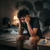年輕男性在臥室床邊展現因非醫療目的盲目服用壯陽藥引發之房事表現焦慮與心魔